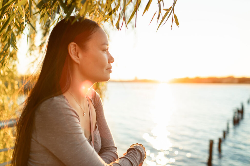 Woman with long hair sitting calmly by a lake at sunset