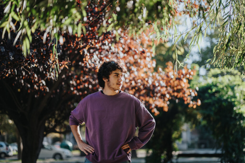 Man in a purple shirt posing in front of bushes
